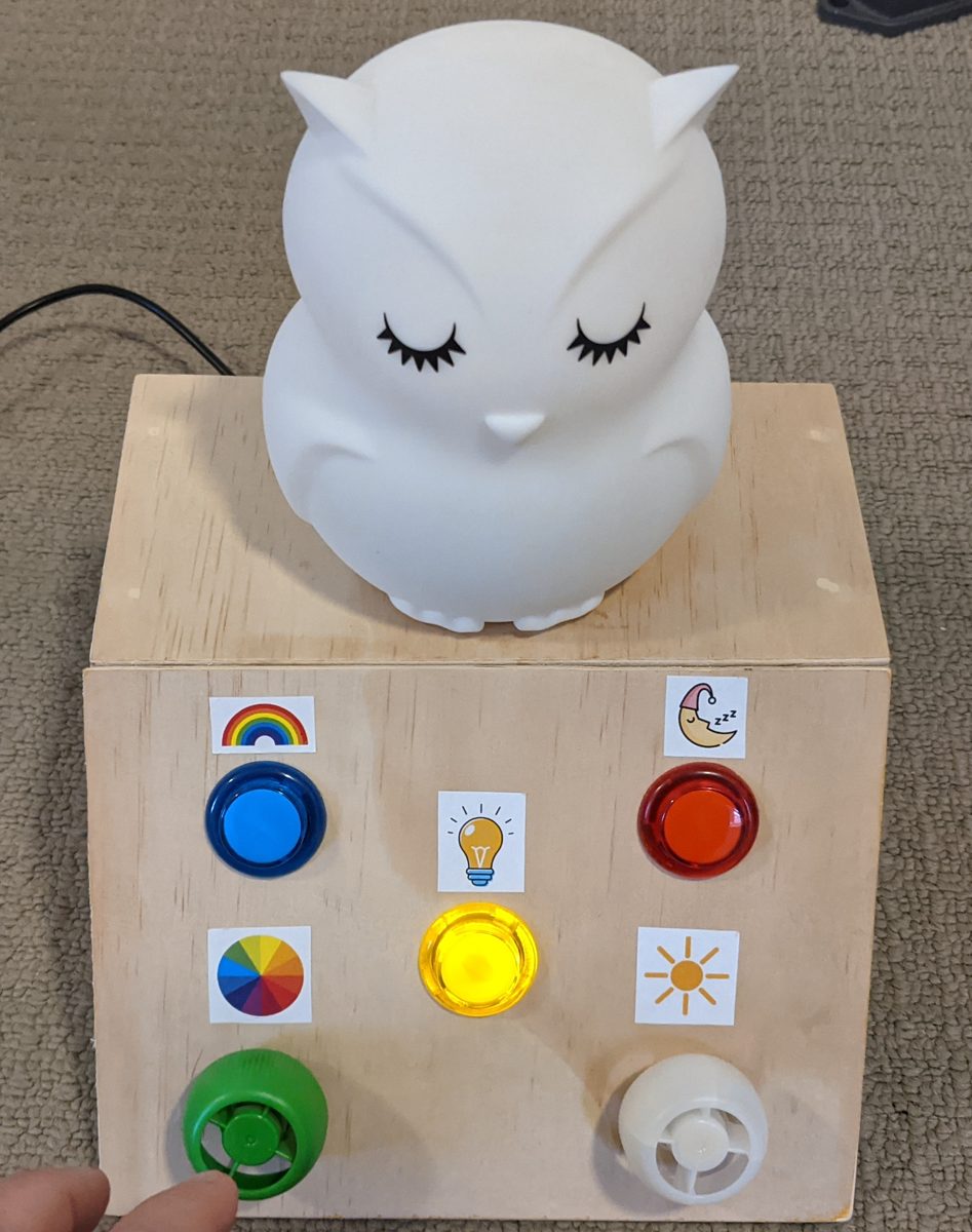 White owl night light sitting on a plywood box with blue, yellow and red buttons and green and white knobs
